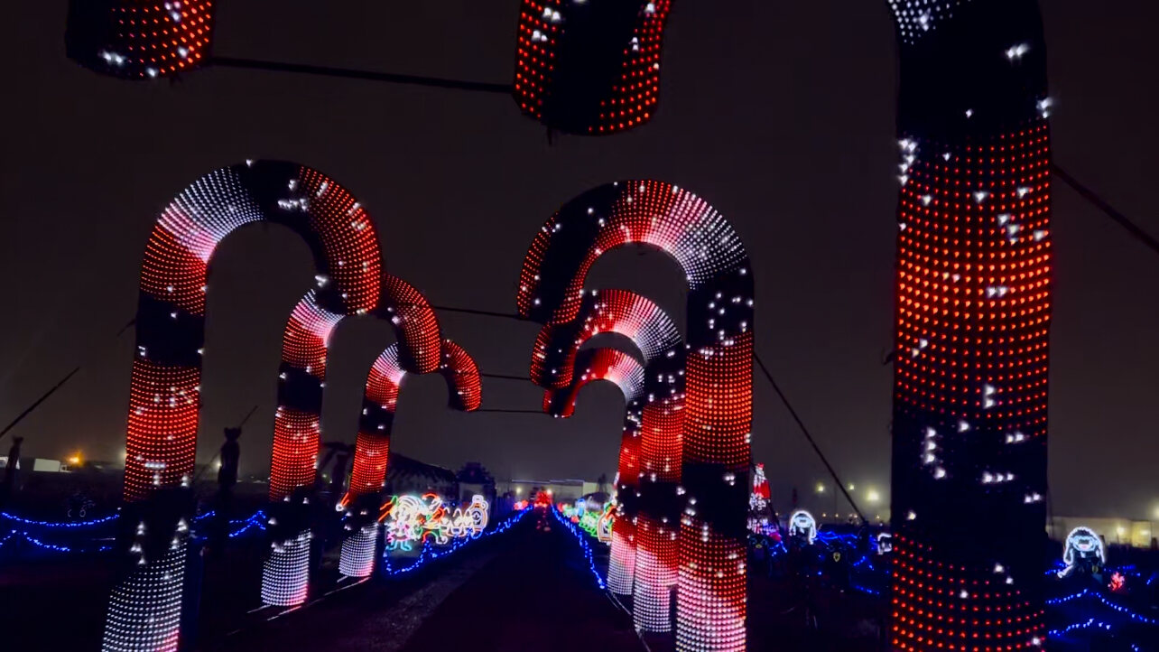 Towering illuminated candy cane arches over a drive-through lane, lit displays either side