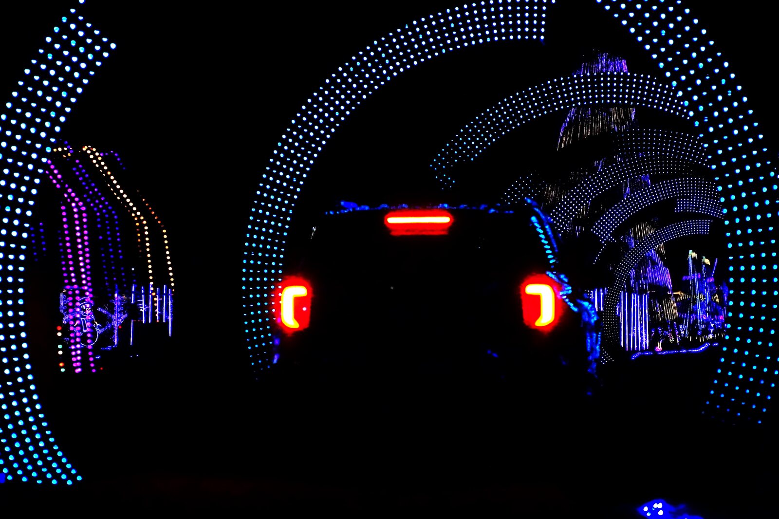 A car driving through a glowing blue arch of lights, taillights bright